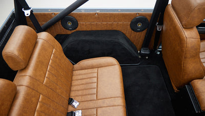 Tan leather rear seat and black carpet floor of Classic Ford Bronco interior with roll cage bars