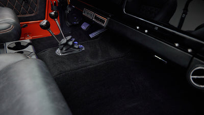 Center floor area with dual gear shifters and black carpet in Classic Ford Bronco with orange door panel.