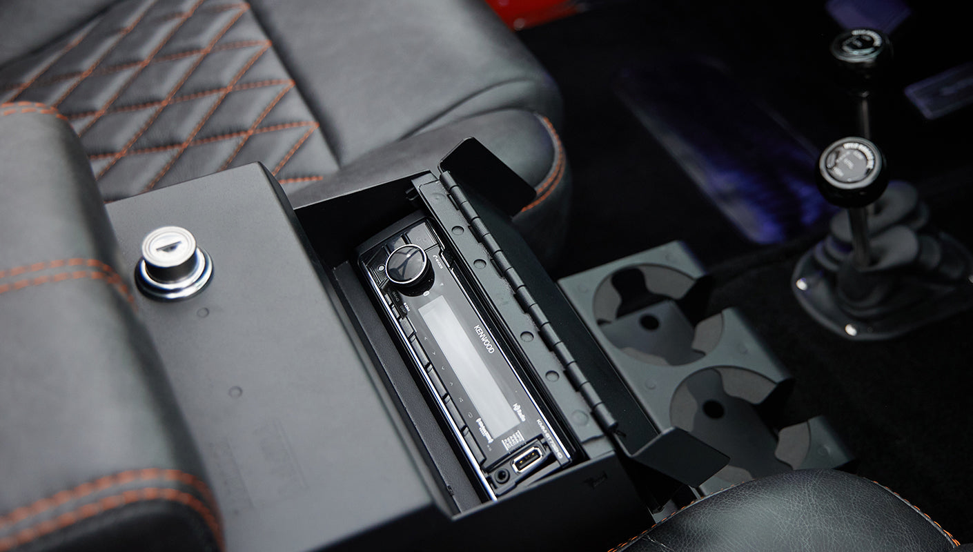 Close-up of a car stereo system and cup holders in console of Classic Ford Bronco with orange and black seat stitching.