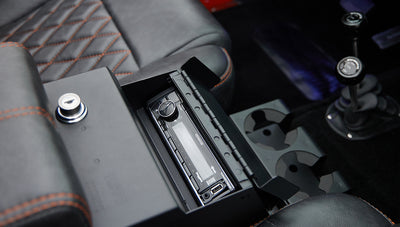 Close-up of a car stereo system and cup holders in console of Classic Ford Bronco with orange and black seat stitching.