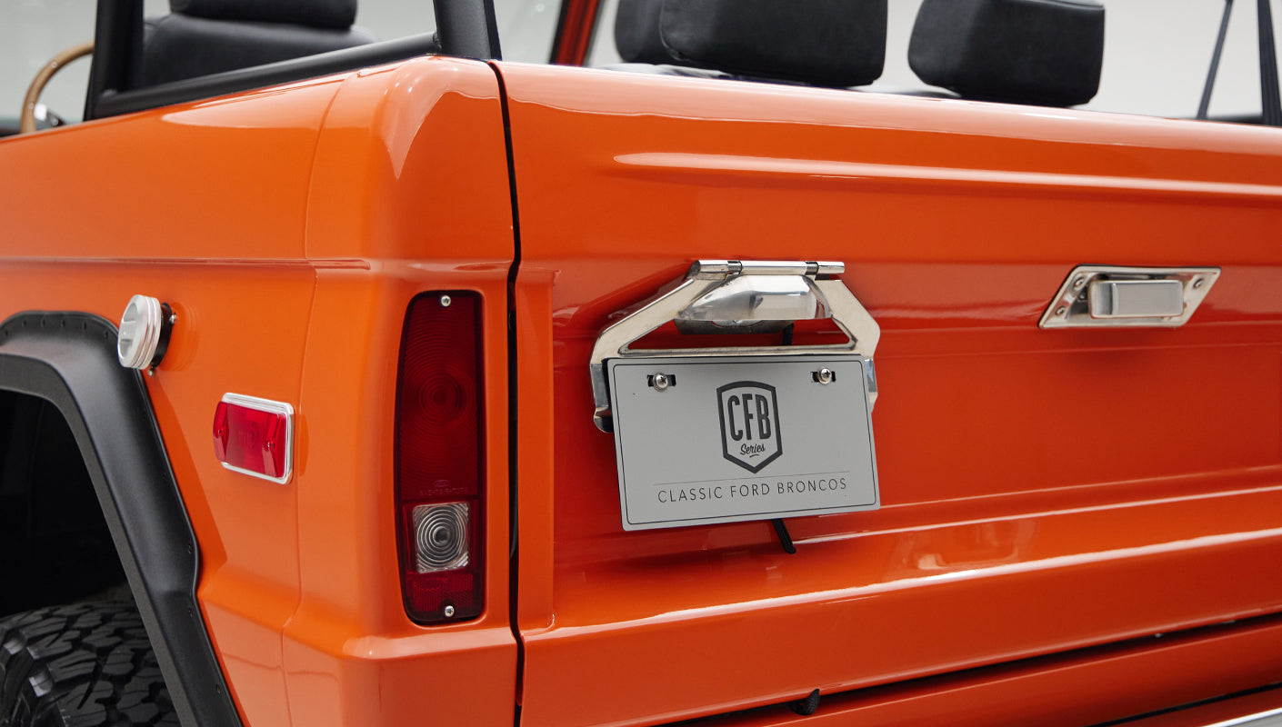 Rear side of orange Classic Ford Bronco including tail lights and license plate holder
