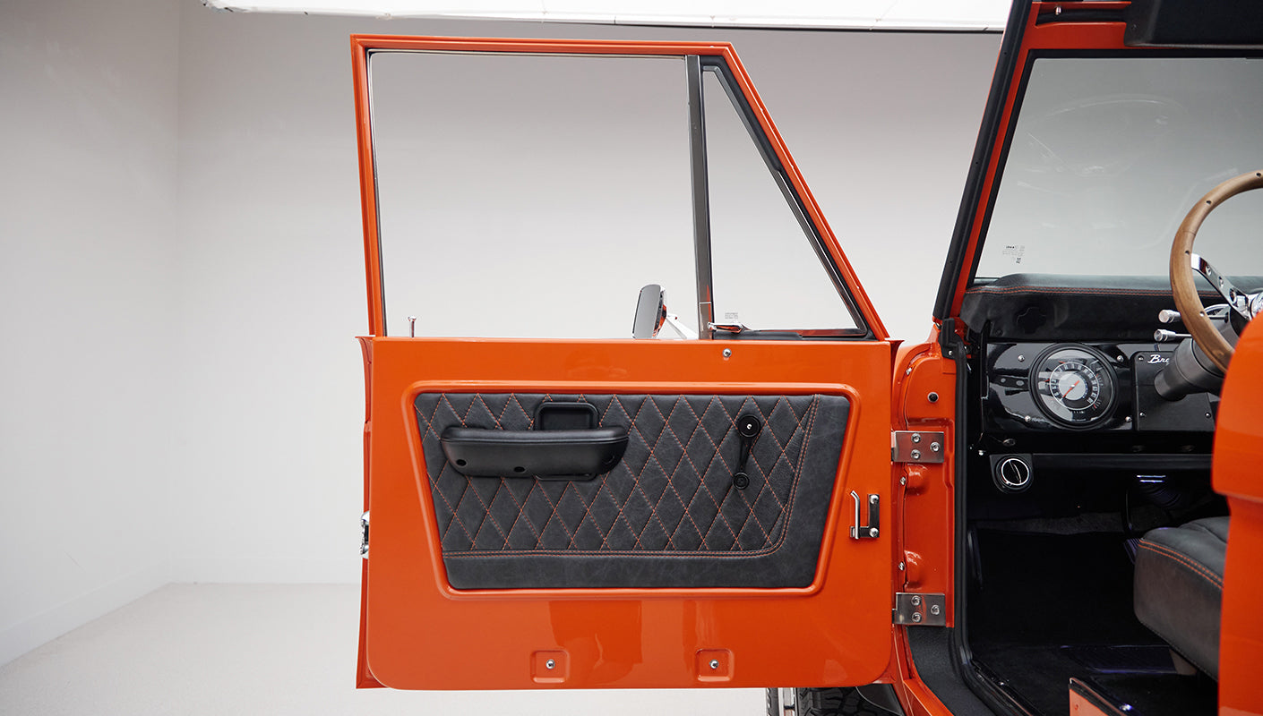 Open orange door showing black quilted interior panel and part of dashboard of Classic Ford Bronco