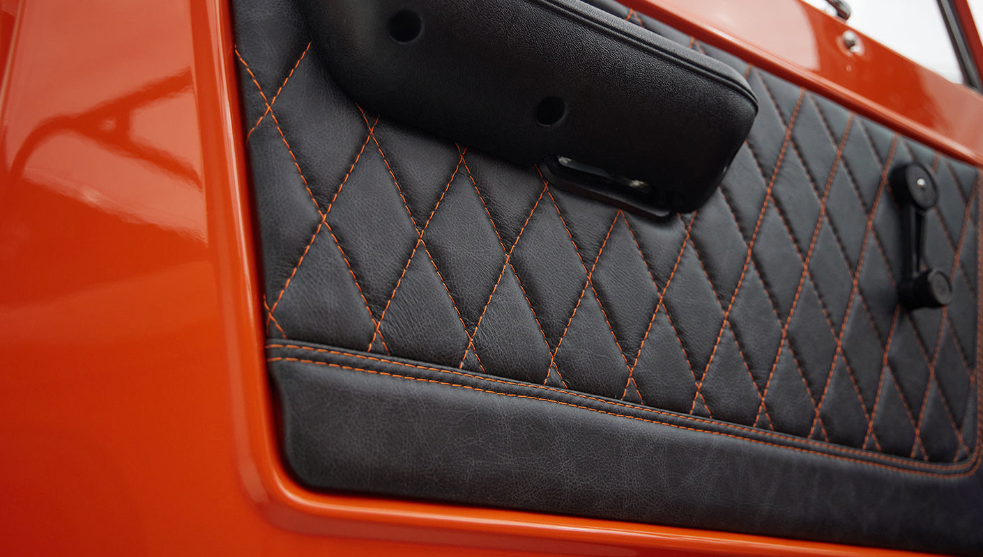 Close-up of quilted black leather door panel with orange stitching in Classic Ford Bronco
