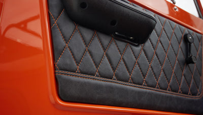 Close-up of quilted black leather door panel with orange stitching in Classic Ford Bronco