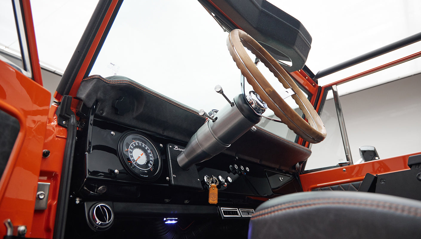 Classic Ford Bronco driver interior highlighting the steering column, dashboard controls, and quilted door panel.