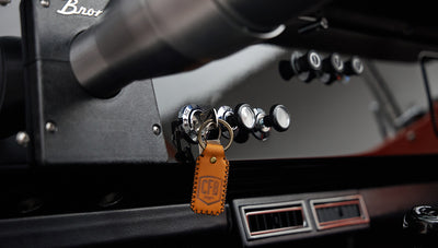 Dashboard close-up with ignition keys attached to leather fob labeled CFB hanging from Classic Ford Bronco steering column.