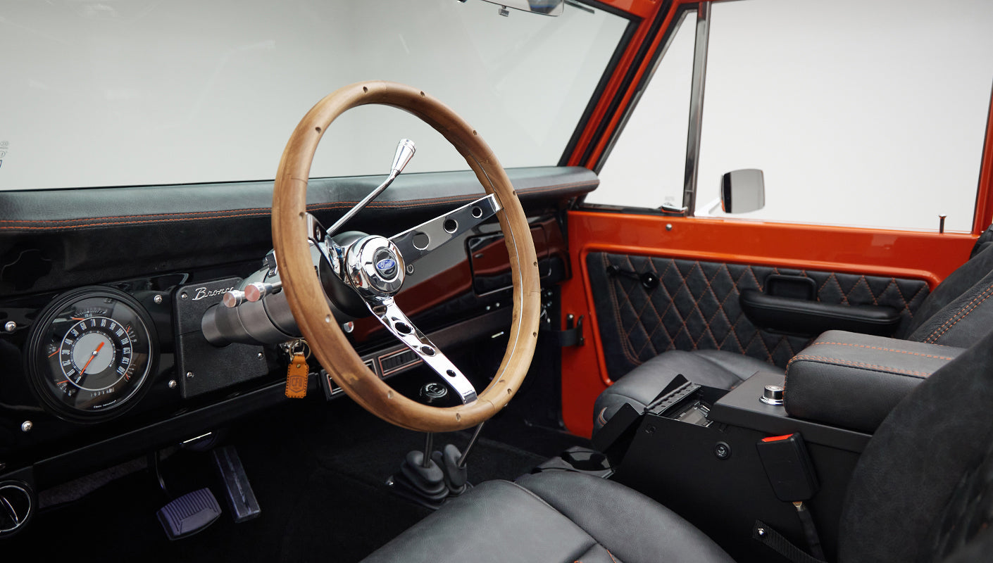 Wood-trimmed steering wheel and instrument panel of Classic Ford Bronco with black and orange interior accents.