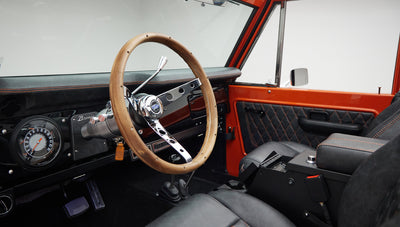 Wood-trimmed steering wheel and instrument panel of Classic Ford Bronco with black and orange interior accents.