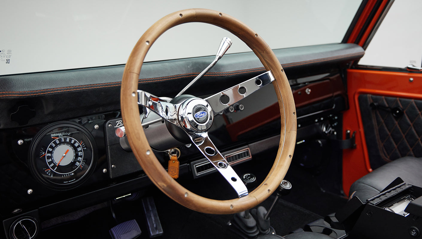 Wooden steering wheel with Ford emblem in Classic Ford Bronco interior showing part of dashboard and center console.