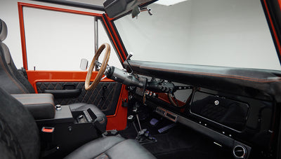 Driver-side interior with wood steering wheel, quilted door panel, and dual gear shifters in Classic Ford Bronco.