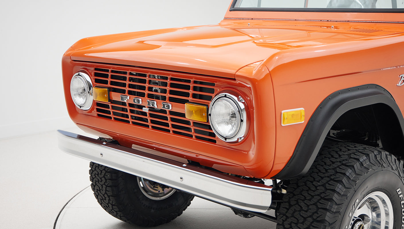 Front view of orange Classic Ford Bronco with chrome bumper and black fender flares