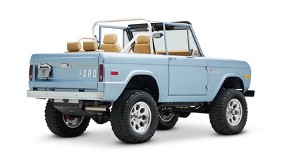 Side and rear views of light blue classic Ford Bronco with open top and extended roll cage on white background