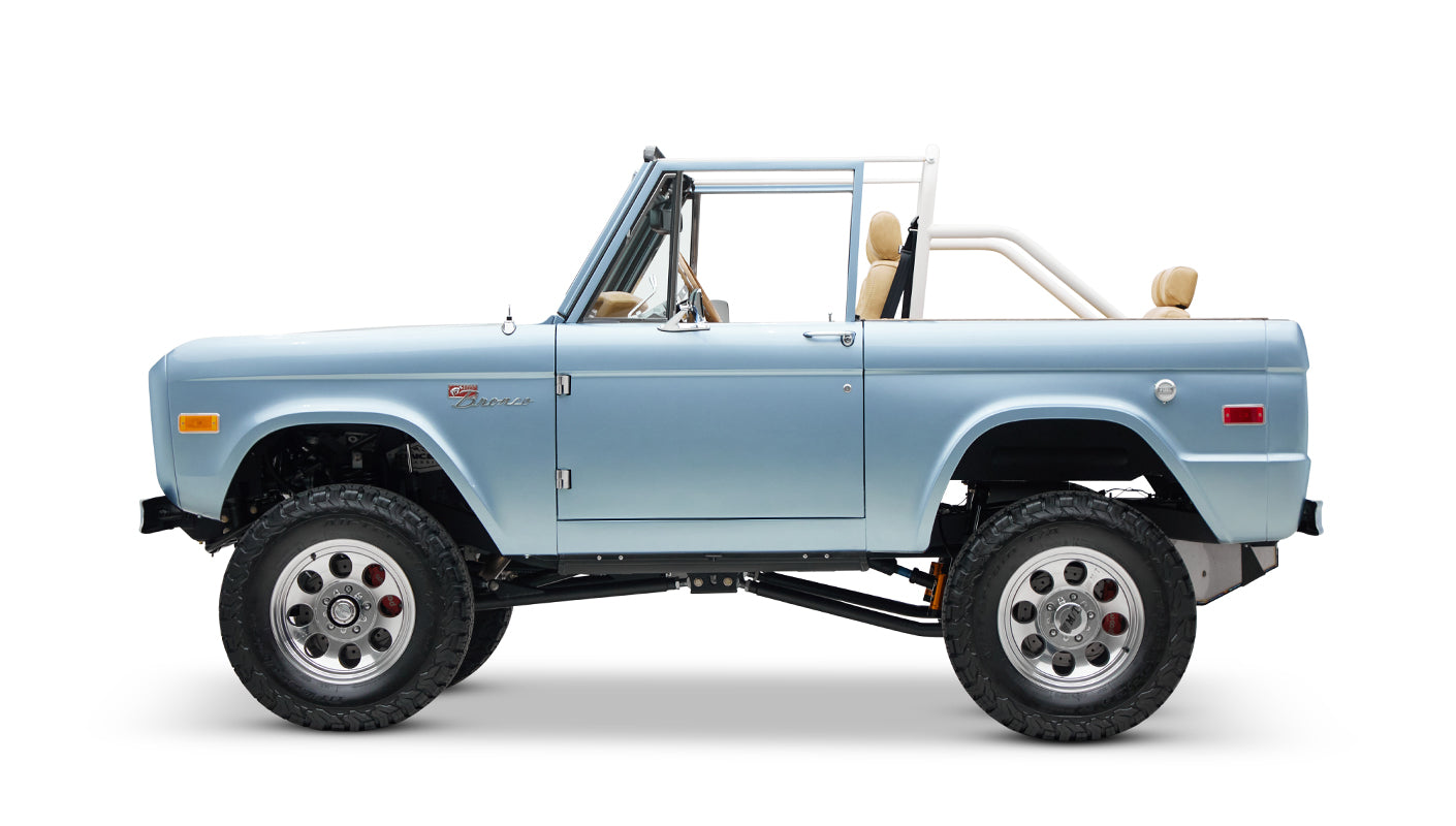 Side view of light blue classic Ford Bronco with lifted suspension and tan seats on white background