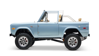 Side view of light blue classic Ford Bronco with lifted suspension and tan seats on white background
