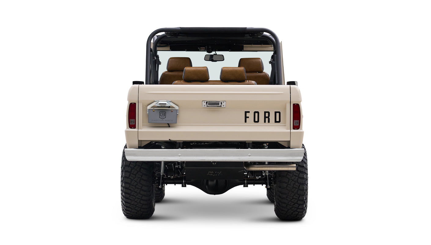 Rear view of cream Classic Ford Bronco with black roll bars, off-road tires, and FORD lettering on tailgate