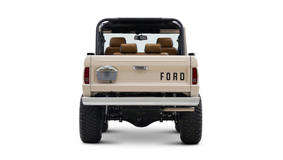 Rear view of cream Classic Ford Bronco with black roll bars, off-road tires, and FORD lettering on tailgate