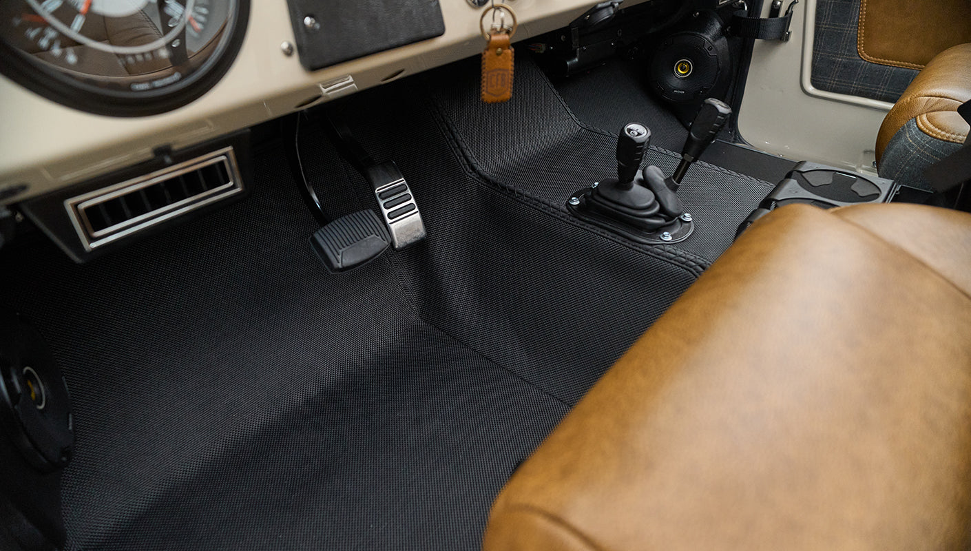 Classic Ford Bronco interior floor area showing pedals, gear levers, and brown leather seat edge