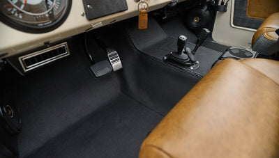Classic Ford Bronco interior floor area showing pedals, gear levers, and brown leather seat edge