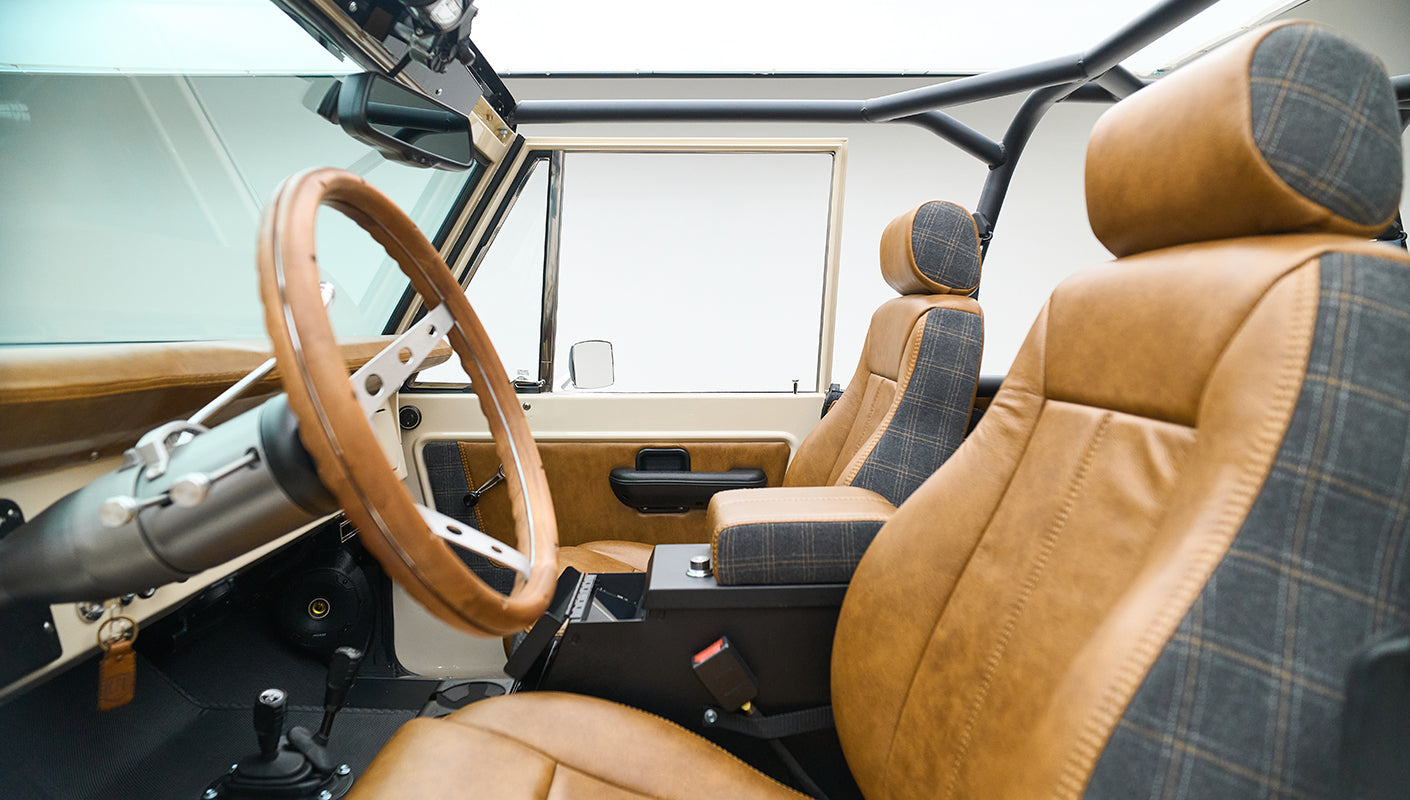 Classic Ford Bronco front seats and dashboard featuring brown leather and plaid upholstery, wooden steering wheel