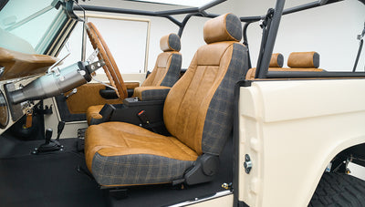 Interior side view of Classic Ford Bronco with brown and plaid front seats and a black roll cage