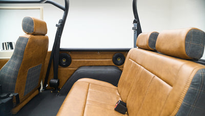 Classic Ford Bronco rear interior showing back seats with brown leather and plaid fabric and speakers