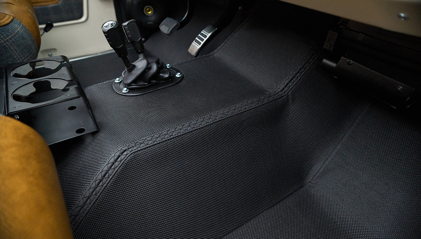 Classic Ford Bronco floor area beside driver seat showing textured floor mats and controls