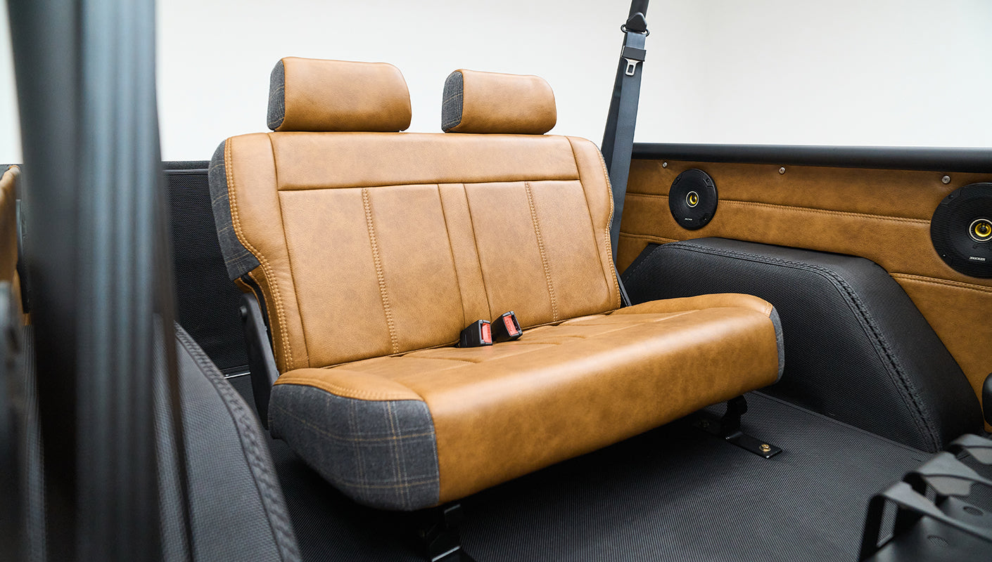 Classic Ford Bronco rear seating area with brown leather and plaid upholstery and black roll cage