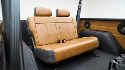 Classic Ford Bronco rear seating area with brown leather and plaid upholstery and black roll cage