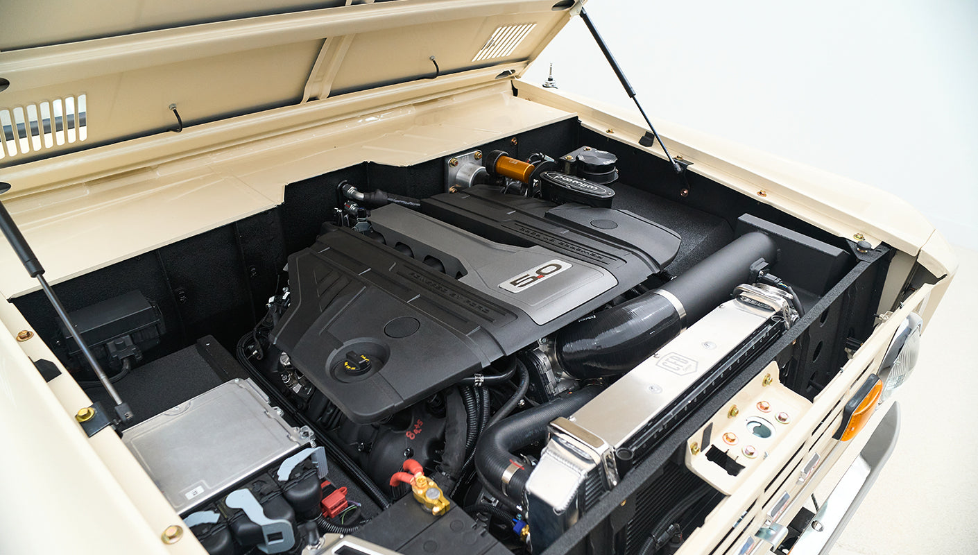 Engine bay showing clean engine with 5.0 badge, black hoses, and radiator