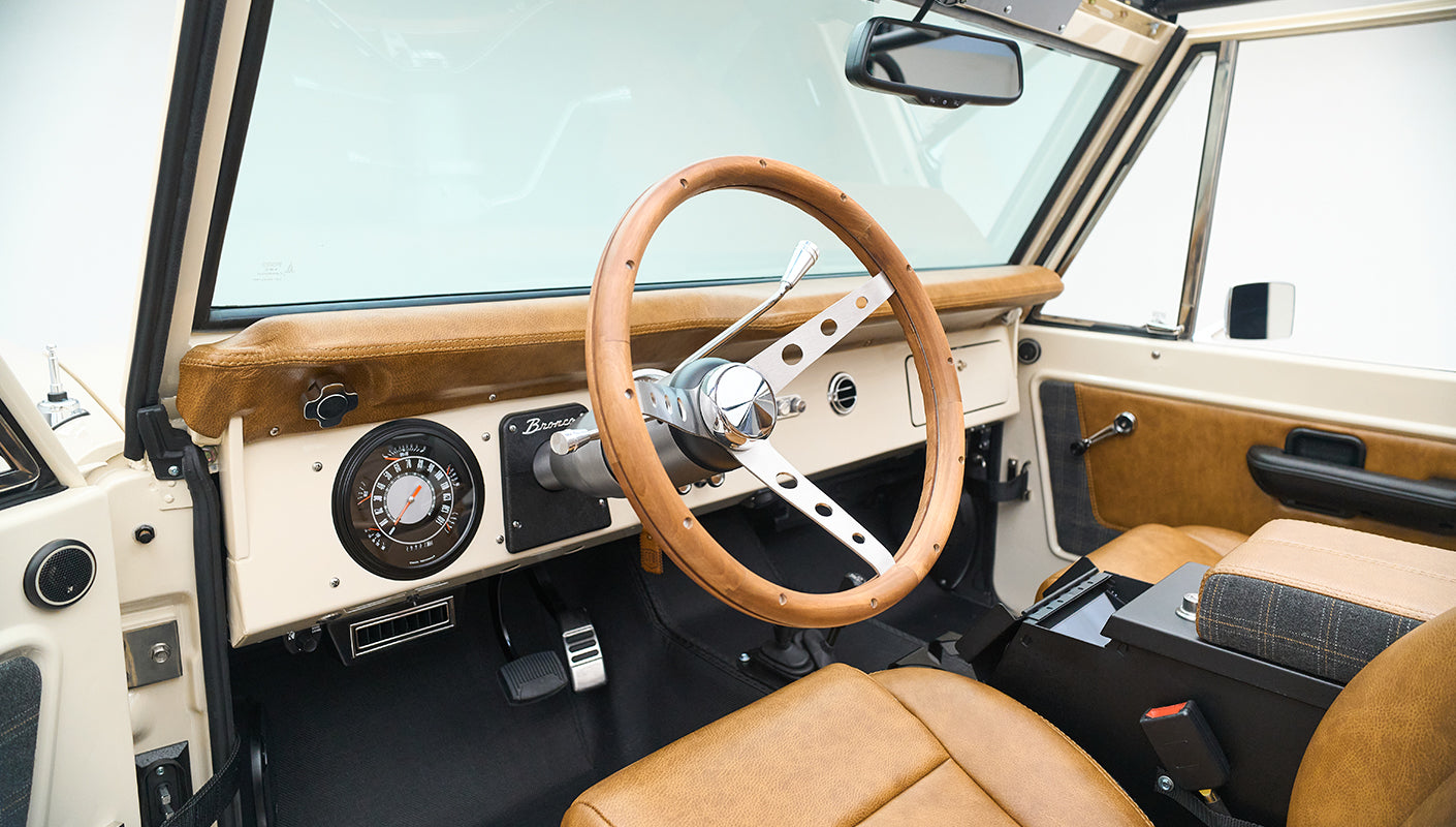 Classic Ford Bronco interior featuring wooden steering wheel and tan upholstery