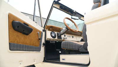 Classic Ford Bronco interior from driver side with open door, showing steering wheel and seats