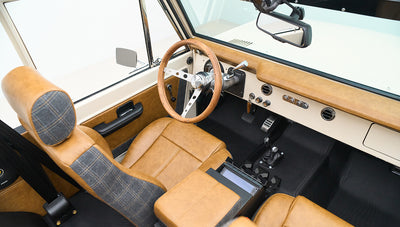 Classic Ford Bronco cockpit with tan leather and plaid seats, steering wheel, and controls