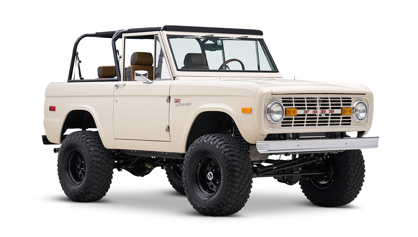 Cream Classic Ford Bronco with black roll bars, off-road tires, and tan seats, angled front side view