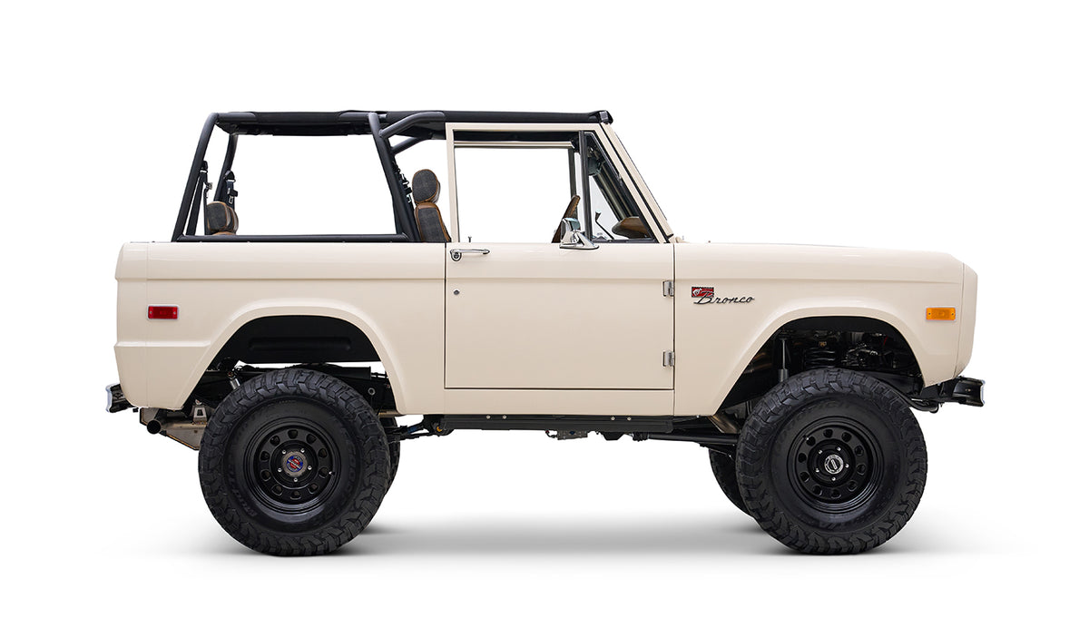 Profile side view of cream Classic Ford Bronco with black roll bars and off-road tires