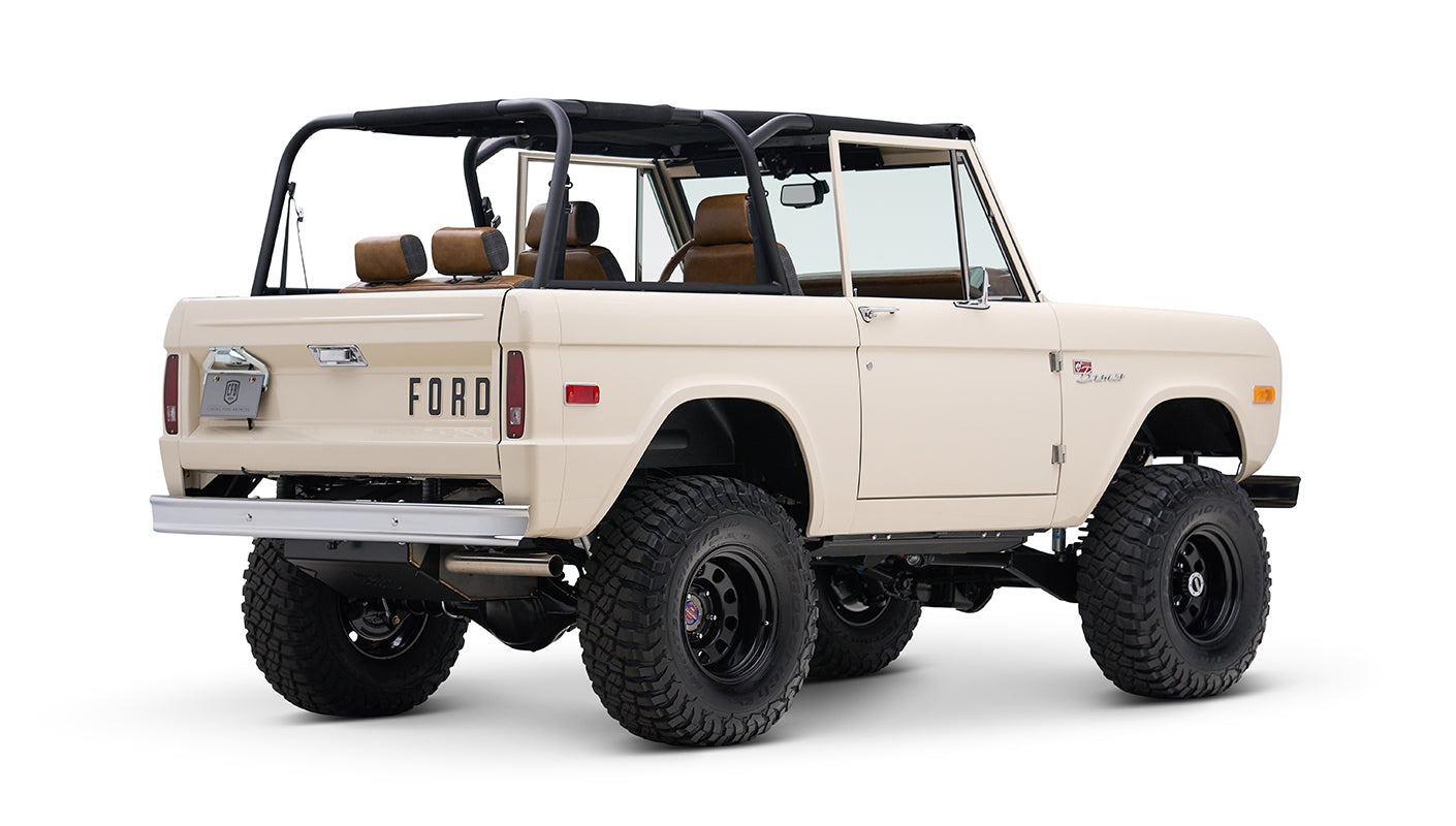 Rear angled view of cream Classic Ford Bronco with black roll bars and off-road tires