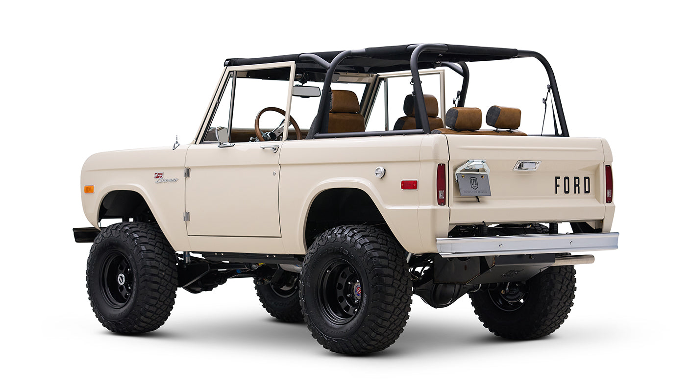 Rear angled view of cream Classic Ford Bronco with black roll bars and off-road tires