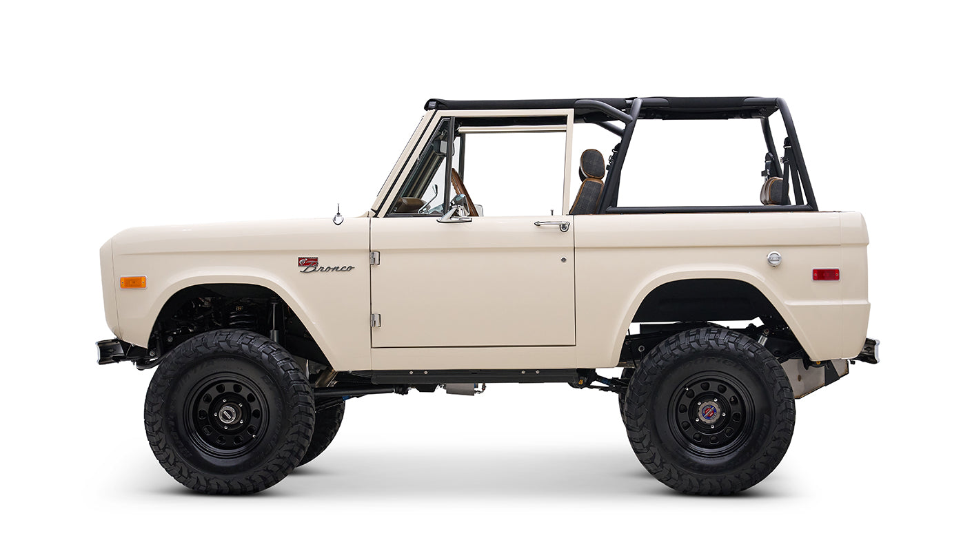 Profile side view of cream Classic Ford Bronco with black roll bars and off-road tires