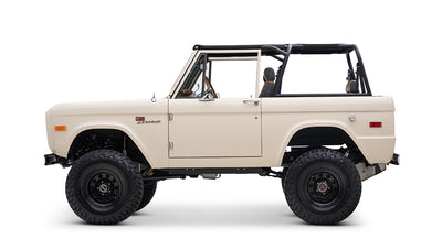 Profile side view of cream Classic Ford Bronco with black roll bars and off-road tires