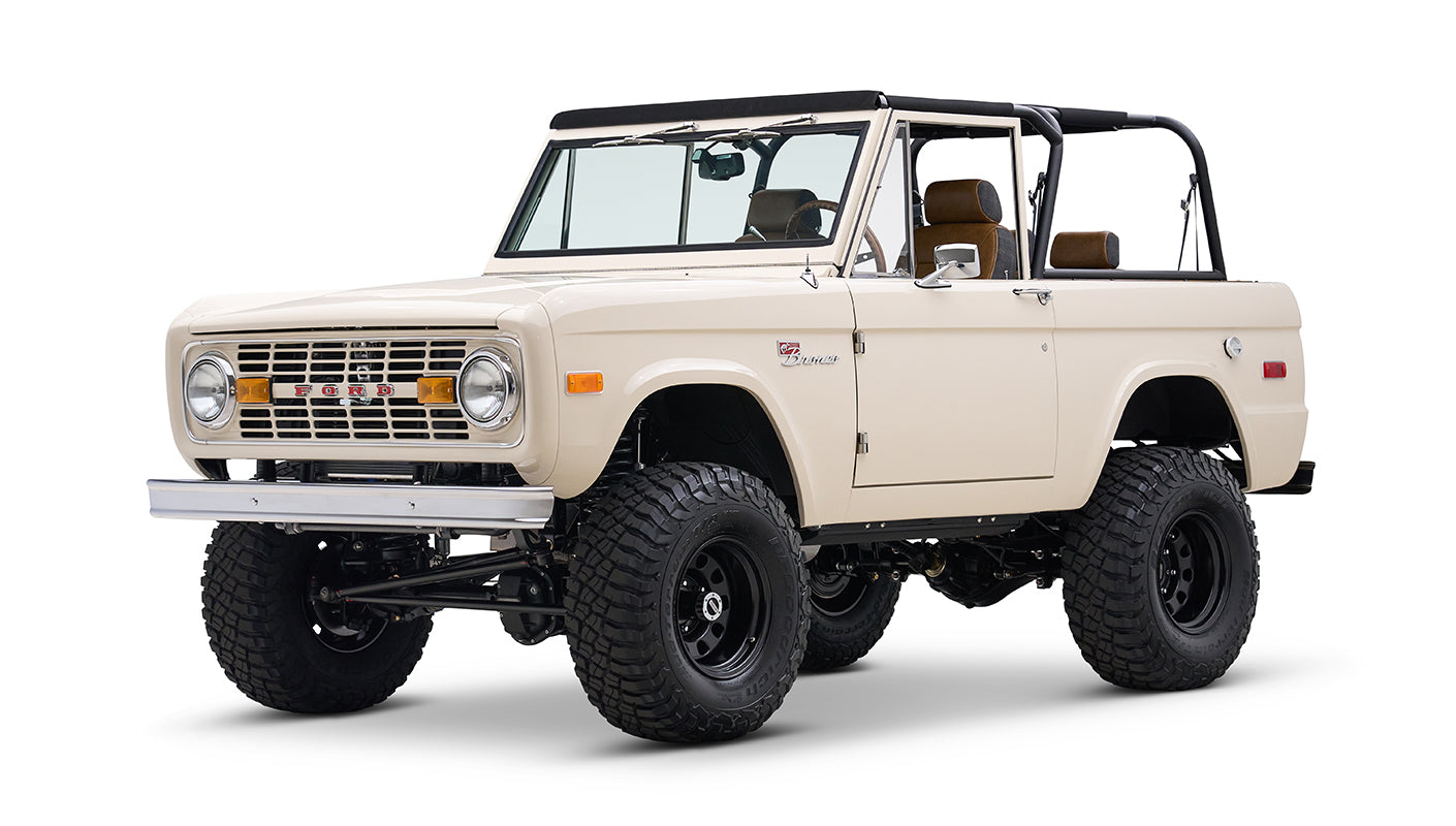 Cream Classic Ford Bronco with black roll bars and large off-road tires, angled front side view