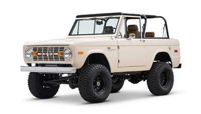 Cream Classic Ford Bronco with black roll bars and large off-road tires, angled front side view