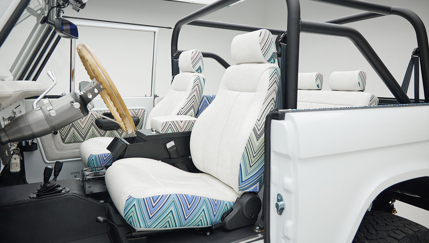View of front seats inside Classic Ford Bronco with white upholstery and patterned accents