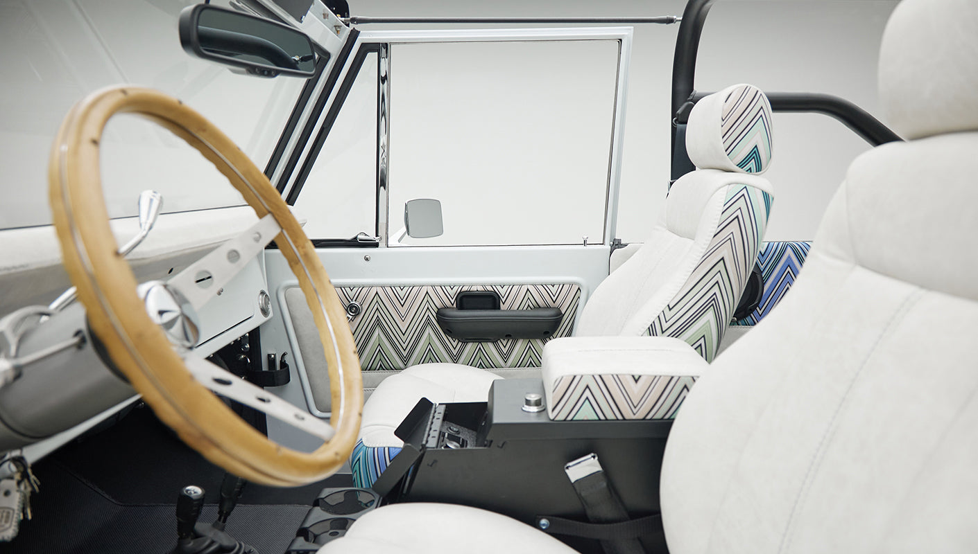 Classic Ford Bronco interior showing white and patterned seats with wooden steering wheel and side door