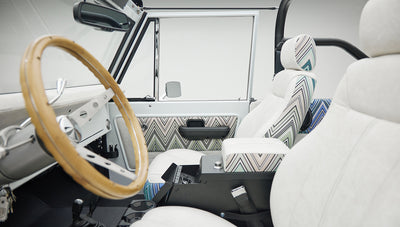 Classic Ford Bronco interior showing white and patterned seats with wooden steering wheel and side door