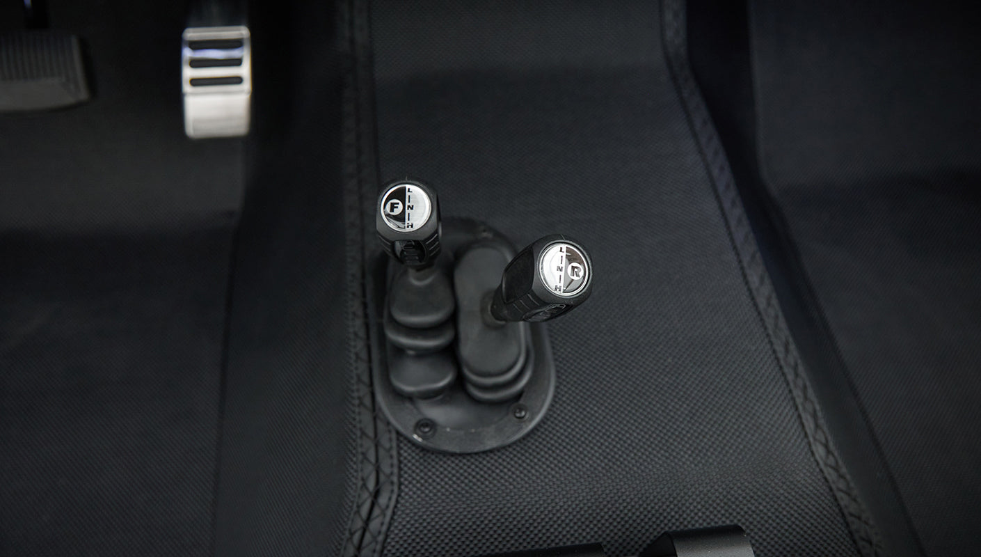 Close-up of gear shift levers on the floor with black textured mat in Classic Ford Bronco