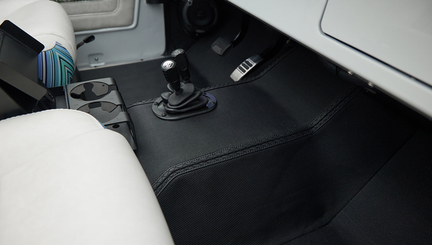 White and blue patterned seat with black floor mat and two gear shift knobs in vehicle interior