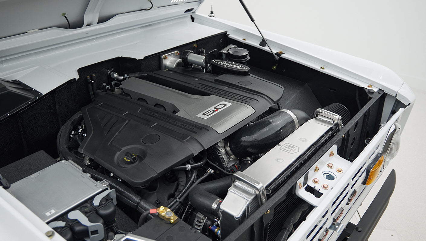 Engine bay with black engine cover labeled 5.0 and surrounding components in white vehicle