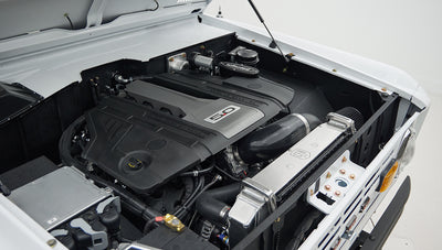 Engine bay with black engine cover labeled 5.0 and surrounding components in white vehicle