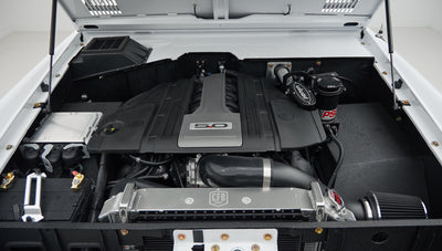 Another view of engine bay showing black engine cover labeled 5.0 and parts with white vehicle exterior