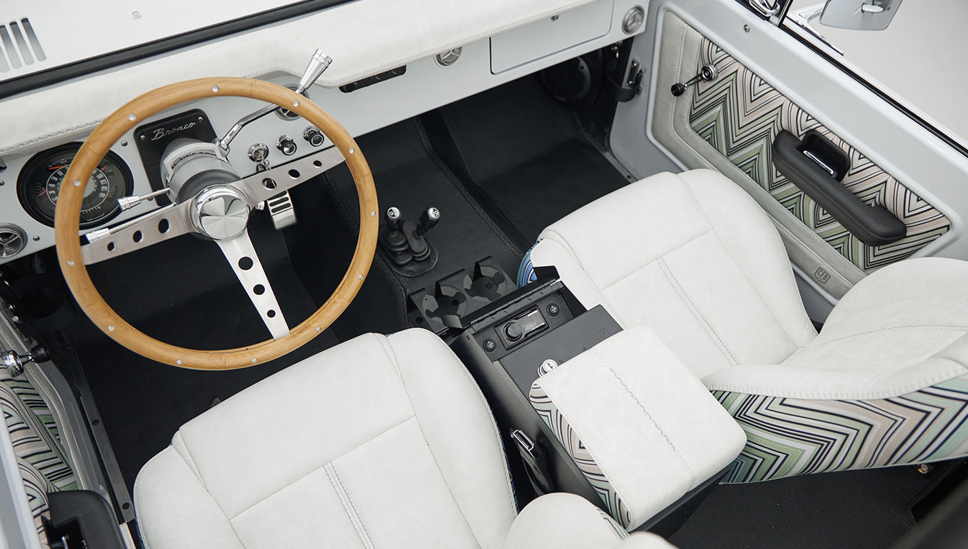 Interior top-down view of Classic Ford Bronco with white seats, wood steering wheel, and patterned door panel