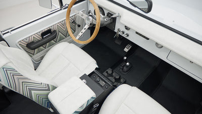 View of Classic Ford Bronco interior showing white upholstered seats, wood steering wheel, and black floor mats